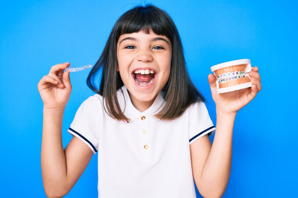 smile child patient holding clear aligners and metal braces